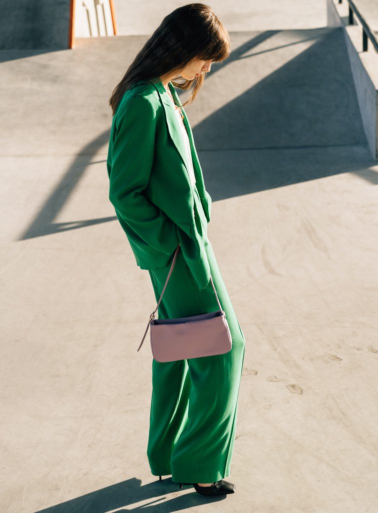 Femme avec un costume vert dans un skate park avec un sac de marque pas cher.