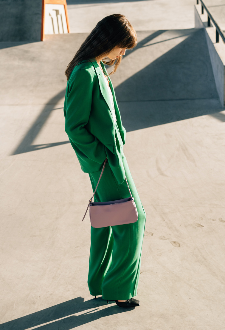 Femme avec un costume vert dans un skate park avec un sac de marque pas cher.