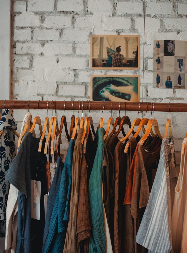 Vêtements sur des cintres sur un rai devant un mur en brique blanc. La photo permet d’illustrer l’article à propos de comment acheter et vendre des vêtements d’occasion.