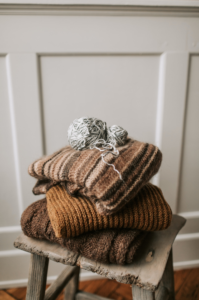 Pile de pulls en laine avec une pelote de laine sur un tabouret en bois afin d’illustrer l’article à propos de l’achat vente de seconde main.