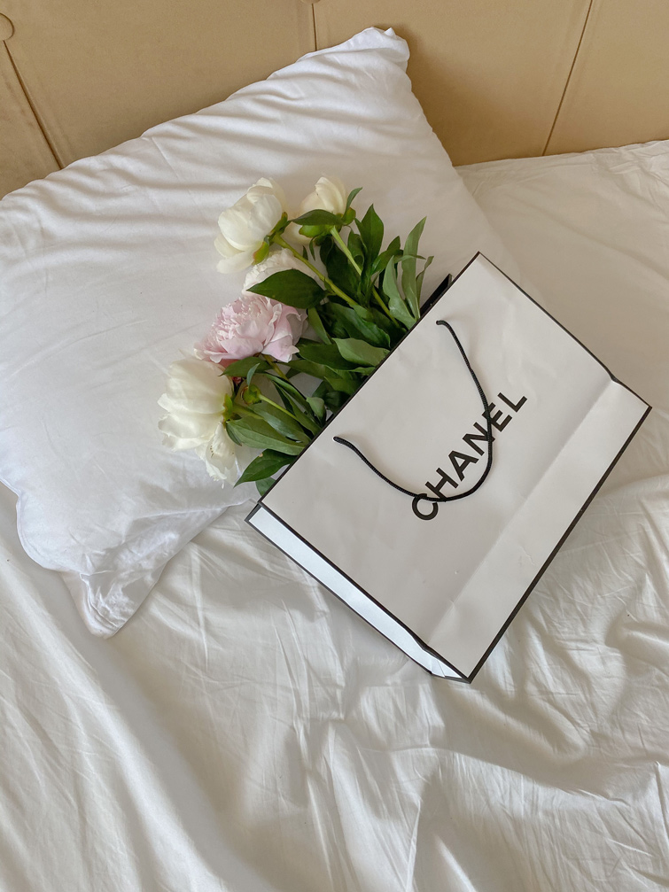 Sac de shopping Chanel sur un lit avec des fleurs à l’intérieur afin d’illustrer l'article les meilleurs magasins de vêtements de luxe d’occasion.