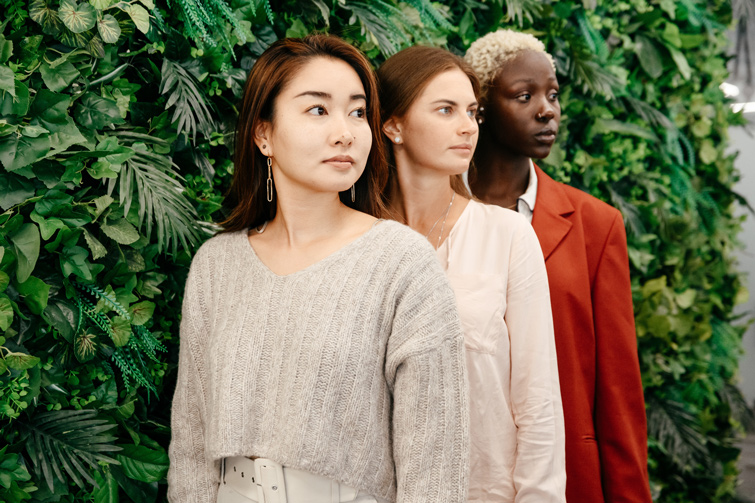 trois femmes habillées élégamment prennent la pose devant un mur végétal. Cette photo illustre le fait que les vêtements responsables sont aussi tendances et modernes.