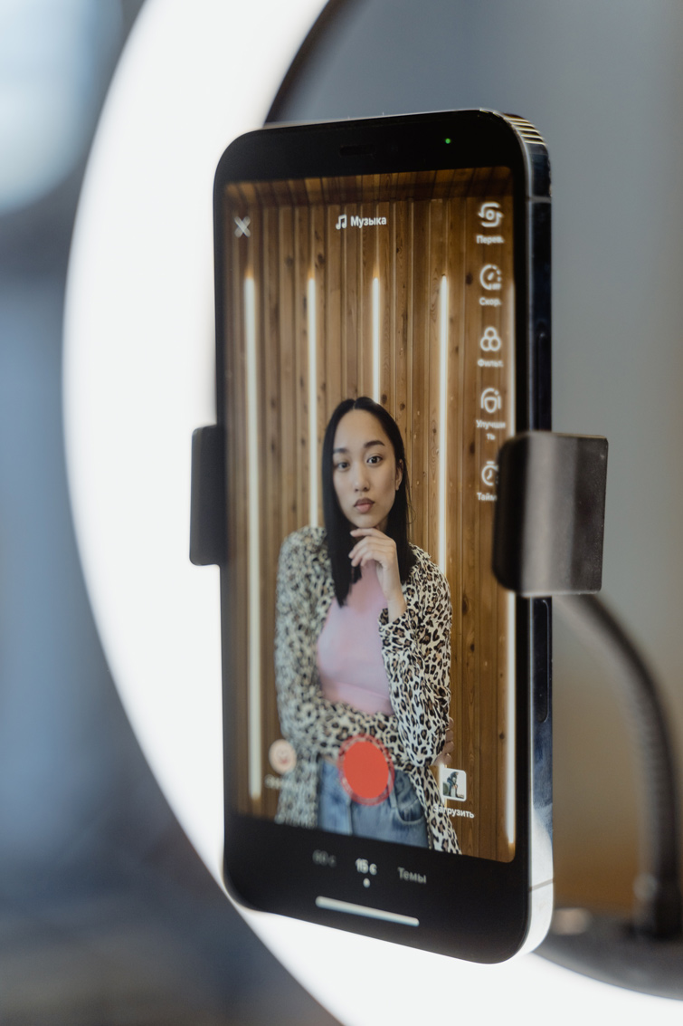 Smartphone sur un gyropode et une lumière de studio filmant une femme brune pour réaliser une vidéo TikTok. Photo d’illustration de notre article sur la guerre entre Instagram vs TikTok.