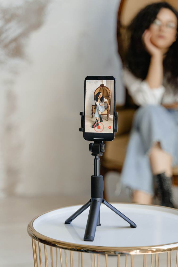 Téléphone sur un gyropode filmant une femme brune assise sur un grand fauteuil. Image d’illustration de notre article sur Instagram vs tiktok.
