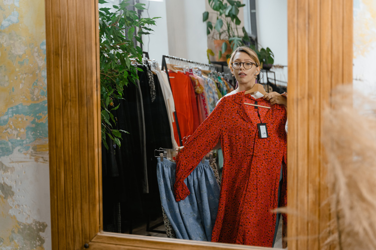 Une femme est dans une boutique de mode écologique, devant un miroir. Elle essaye une robe rouge.