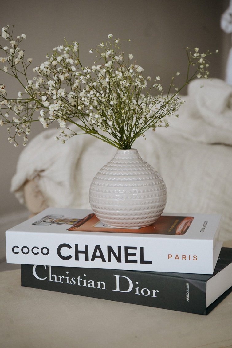 Des livres Chanel et Dior sont empilés dessous un pot avec des fleurs afin d’illustrer l’influence d’Instagram sur la mode et le luxe.